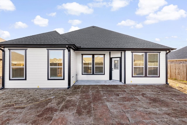 back of property with a patio area, a shingled roof, and fence