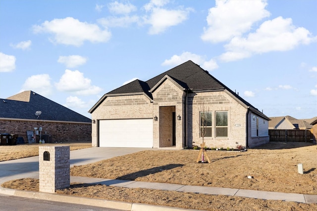 french country inspired facade featuring a garage, brick siding, driveway, and fence