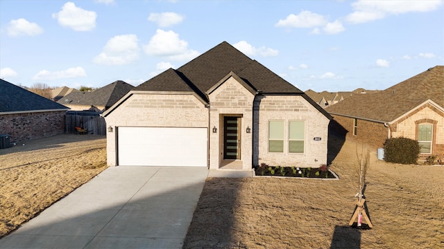 french country style house featuring driveway, a garage, a shingled roof, cooling unit, and brick siding