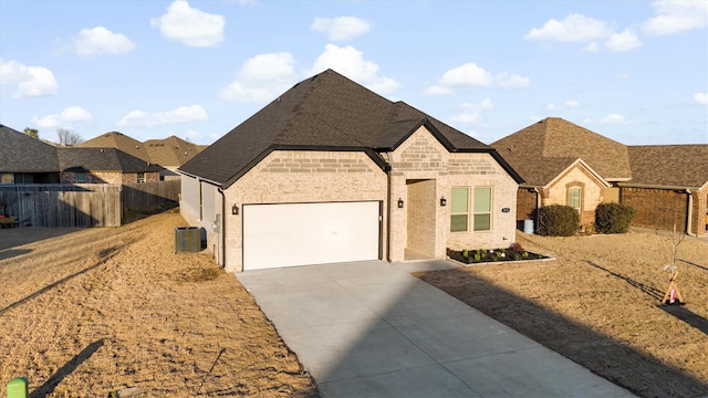 french country inspired facade with an attached garage, central AC, brick siding, fence, and concrete driveway