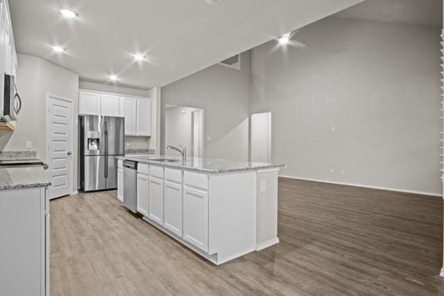 kitchen with a center island with sink, stainless steel appliances, white cabinets, a sink, and light wood-type flooring