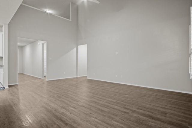 unfurnished living room featuring dark wood-type flooring, a towering ceiling, and baseboards