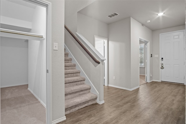 foyer entrance with baseboards, stairs, visible vents, and wood finished floors