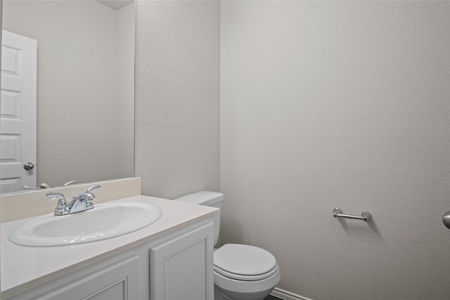 half bath featuring a textured wall, vanity, and toilet