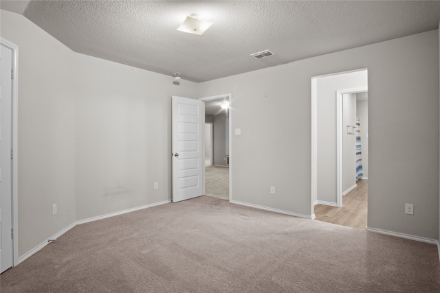 empty room featuring light carpet, a textured ceiling, visible vents, and baseboards