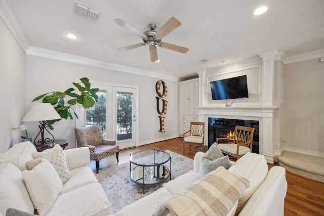 living room featuring ornamental molding, wood finished floors, a glass covered fireplace, and visible vents