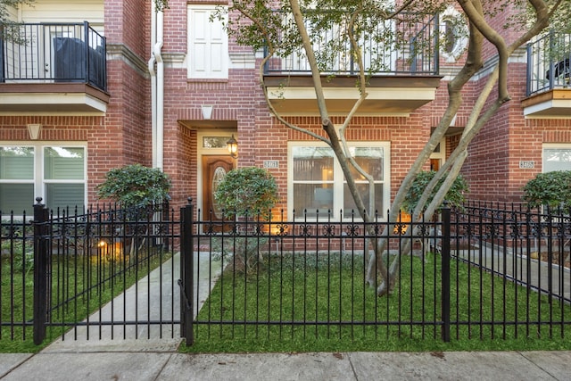 view of front facade featuring brick siding, a fenced front yard, and a balcony