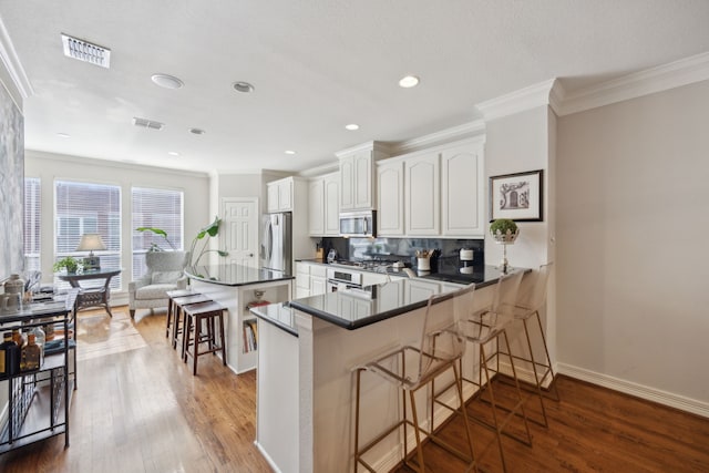 kitchen featuring a breakfast bar, stainless steel appliances, dark countertops, visible vents, and white cabinetry