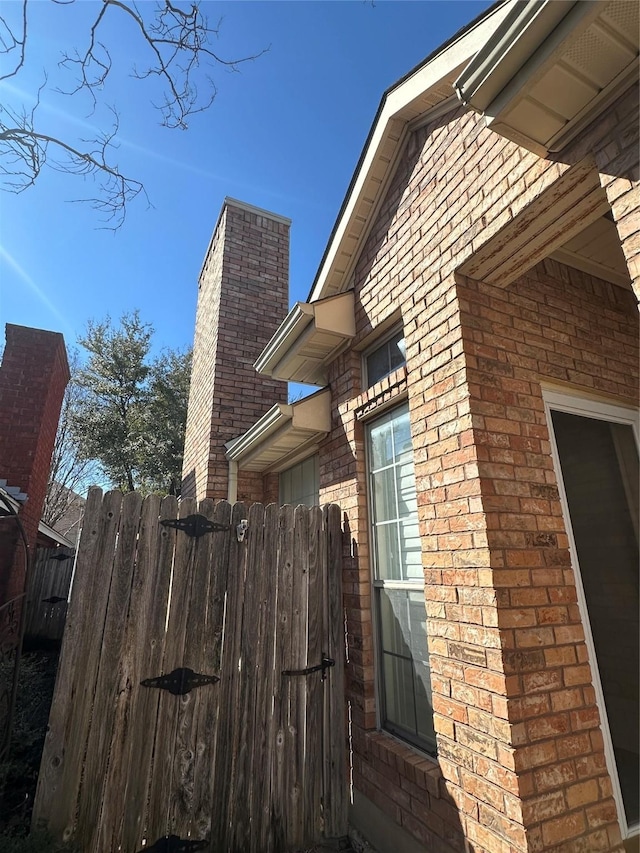 view of home's exterior featuring a chimney, fence, and brick siding