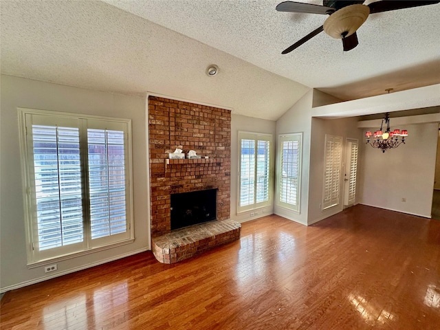 unfurnished living room featuring a brick fireplace, ceiling fan, vaulted ceiling, a textured ceiling, and wood finished floors