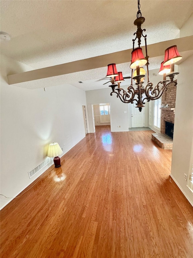 unfurnished dining area featuring a textured ceiling, a fireplace, visible vents, and wood finished floors