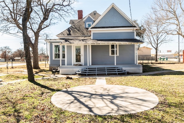 rear view of property featuring a porch, fence, a yard, roof with shingles, and a chimney