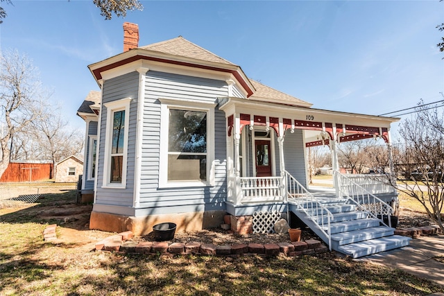 view of front of home with a porch, roof with shingles, fence, and a chimney