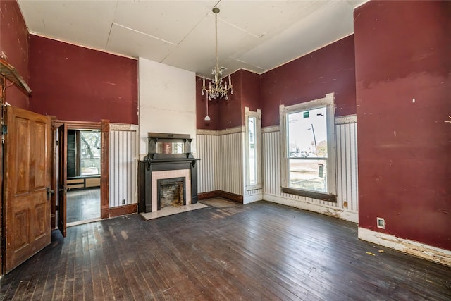 unfurnished living room featuring a chandelier, hardwood / wood-style flooring, a wainscoted wall, a high ceiling, and a tiled fireplace