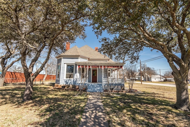 victorian home with a chimney, roof with shingles, covered porch, fence, and a front yard