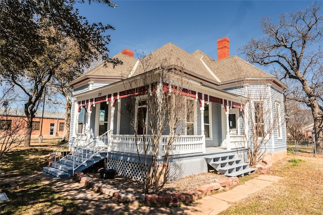 view of front of house with roof with shingles, a porch, a chimney, and fence