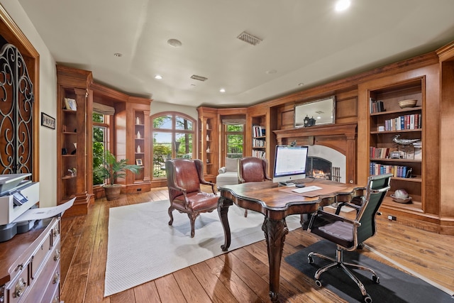 home office with hardwood / wood-style floors, a warm lit fireplace, built in features, and recessed lighting