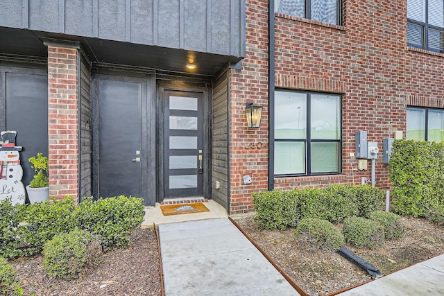 doorway to property featuring board and batten siding and brick siding