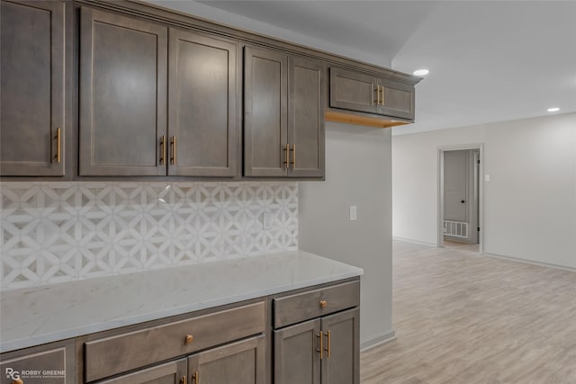 kitchen with tasteful backsplash, light stone counters, dark brown cabinets, light wood-type flooring, and recessed lighting