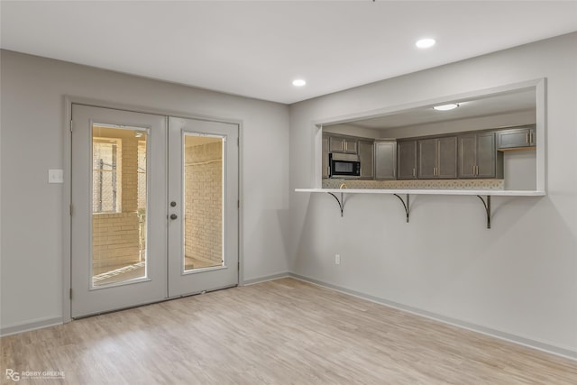 interior space with stainless steel microwave, a breakfast bar, light countertops, french doors, and light wood-type flooring