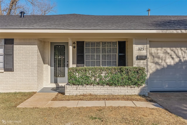 entrance to property featuring roof with shingles, brick siding, and an attached garage