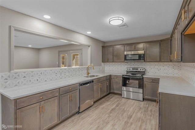 kitchen featuring stainless steel appliances, light countertops, backsplash, light wood-style floors, and a sink