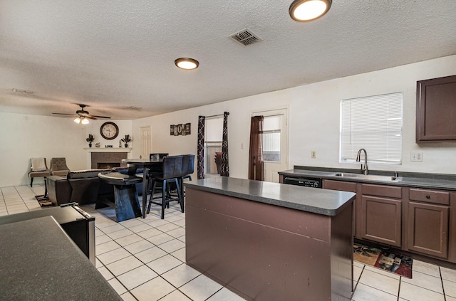 kitchen with dark countertops, a kitchen island, visible vents, and a sink