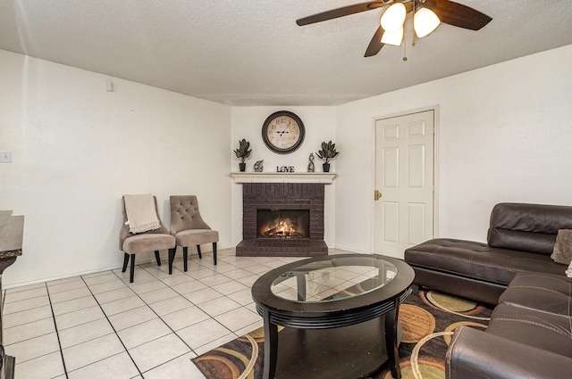 living area featuring a ceiling fan, a brick fireplace, a textured ceiling, and light tile patterned floors