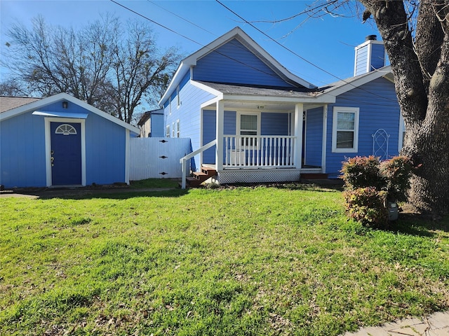 view of front of home featuring a chimney, an outbuilding, covered porch, fence, and a front lawn