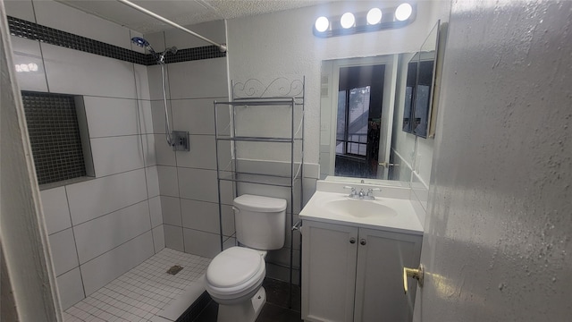 full bath featuring a textured wall, tiled shower, vanity, and toilet