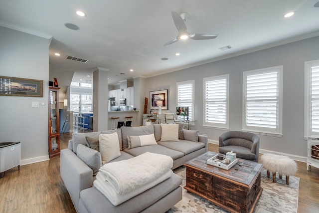 living area with baseboards, wood finished floors, visible vents, and ornamental molding