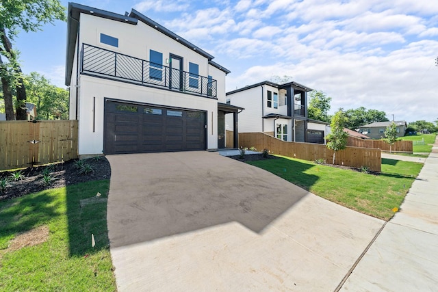 modern home with a balcony, fence, driveway, stucco siding, and a front yard