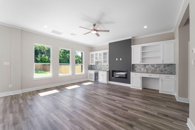 unfurnished living room featuring ornamental molding, beverage cooler, built in desk, and baseboards