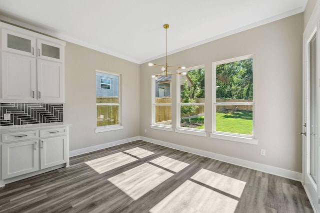 unfurnished dining area with crown molding, an inviting chandelier, dark wood finished floors, and baseboards