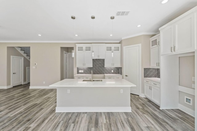 kitchen with a center island with sink, visible vents, light wood-style floors, glass insert cabinets, and baseboards