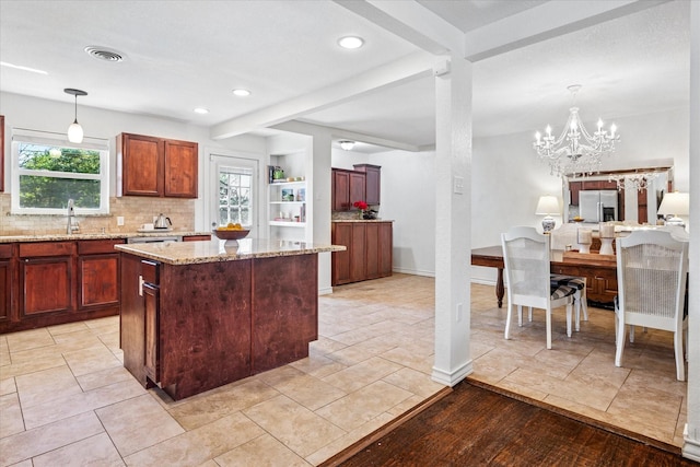 kitchen with stainless steel fridge, tasteful backsplash, visible vents, light stone counters, and a center island