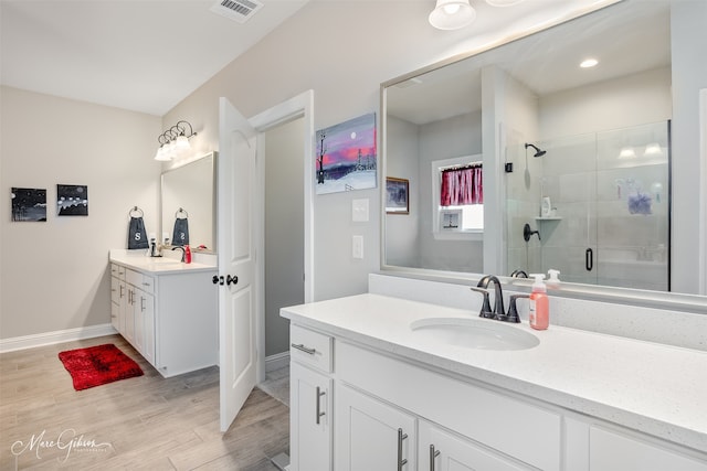 bathroom with a stall shower, visible vents, wood finished floors, a sink, and two vanities