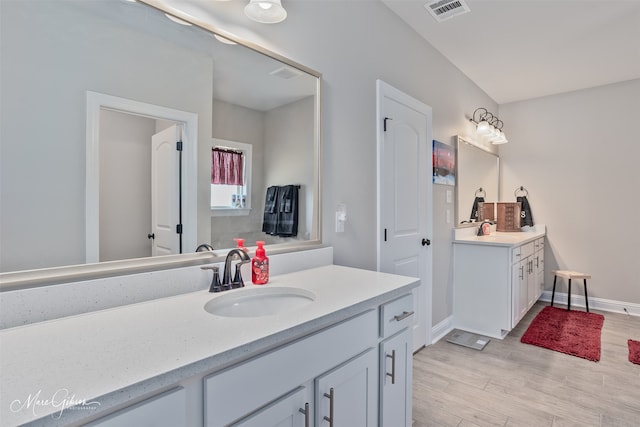 full bath featuring visible vents, two vanities, a sink, and wood finished floors