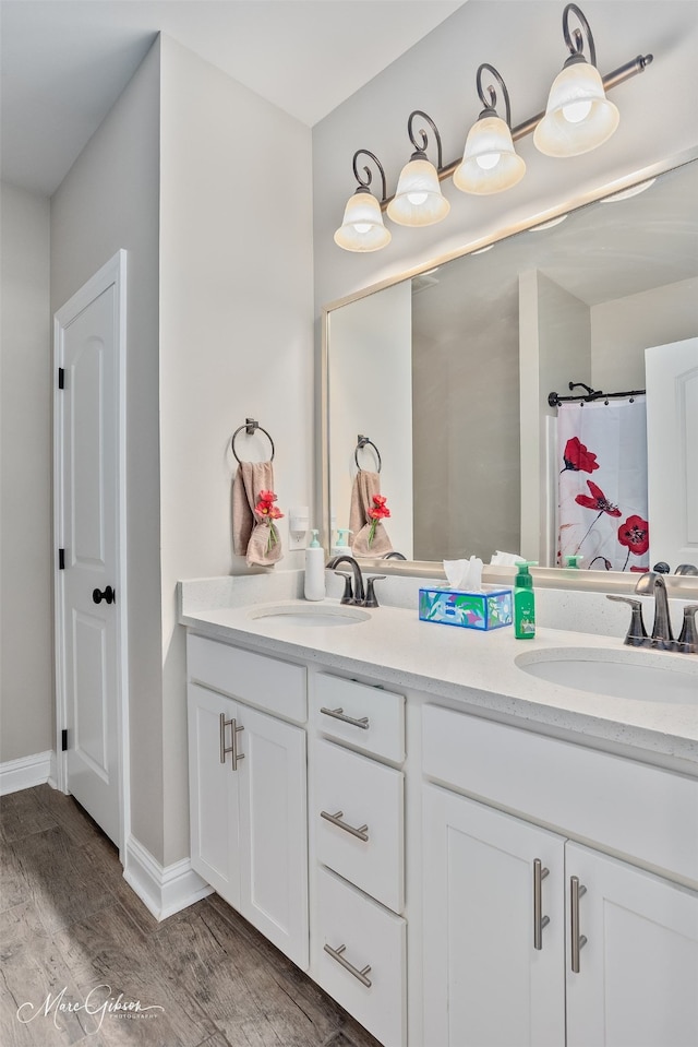 bathroom with double vanity, wood finished floors, a sink, and baseboards