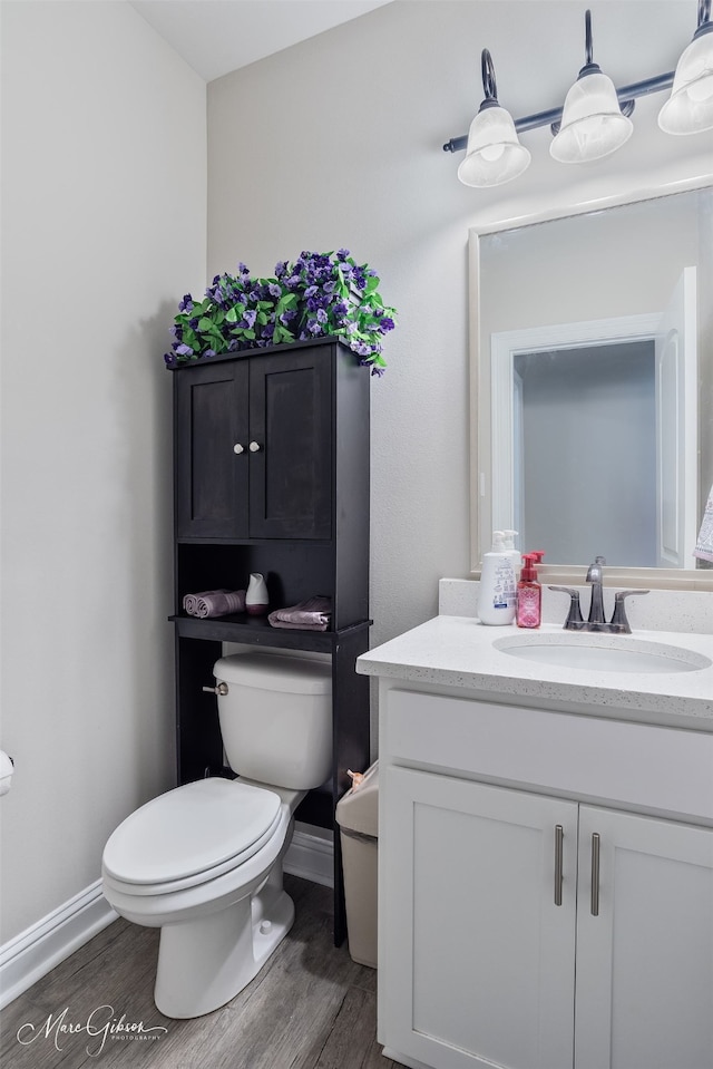 half bath with baseboards, vanity, toilet, and wood finished floors