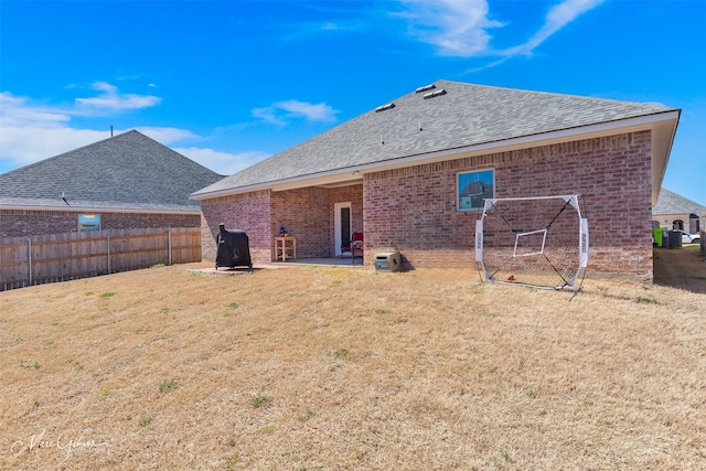 back of property with roof with shingles, fence, a yard, a patio area, and brick siding