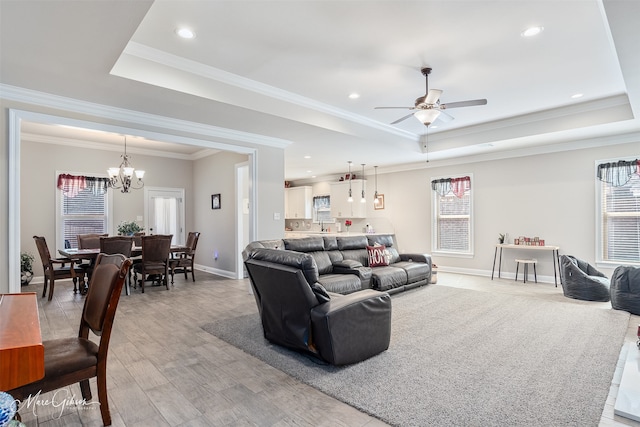 living area with light wood-type flooring, a tray ceiling, baseboards, and ceiling fan with notable chandelier