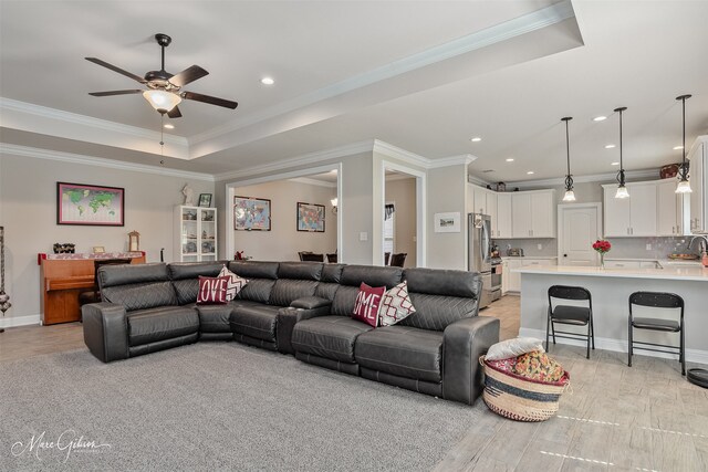 living area featuring a raised ceiling, a ceiling fan, ornamental molding, light wood-style floors, and recessed lighting