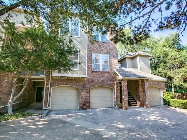 multi unit property with brick siding, a shingled roof, stairway, an attached garage, and driveway