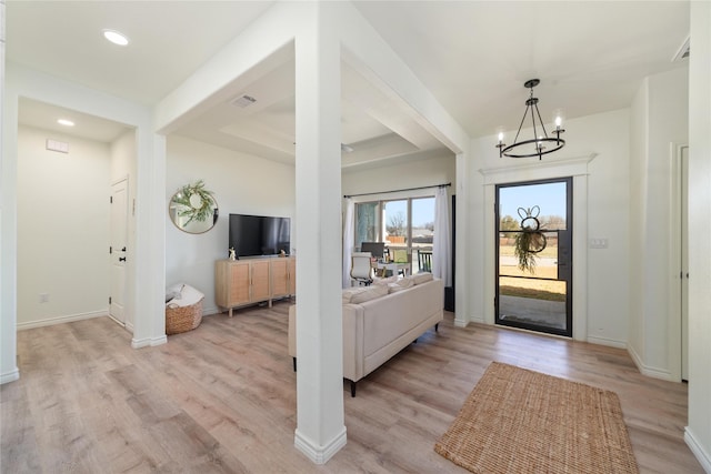 entrance foyer featuring a notable chandelier, a tray ceiling, baseboards, and light wood-style floors