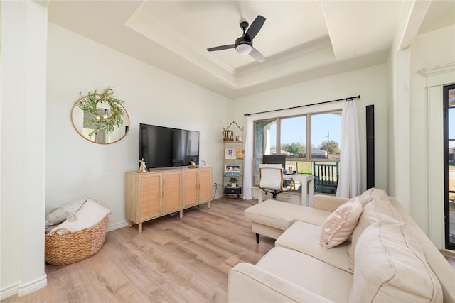 living room featuring a ceiling fan, baseboards, light wood-style floors, a raised ceiling, and crown molding