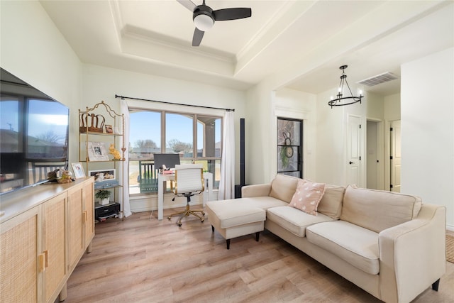 living area with light wood finished floors, visible vents, a tray ceiling, crown molding, and ceiling fan with notable chandelier