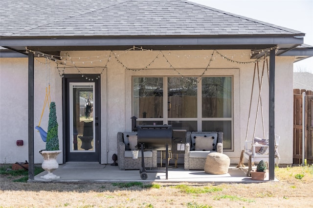 property entrance featuring stucco siding, a patio area, fence, and roof with shingles