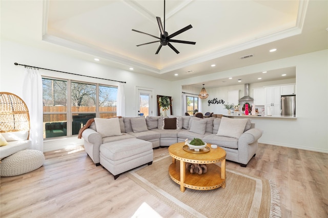 living area with ceiling fan, recessed lighting, visible vents, light wood-type flooring, and a raised ceiling