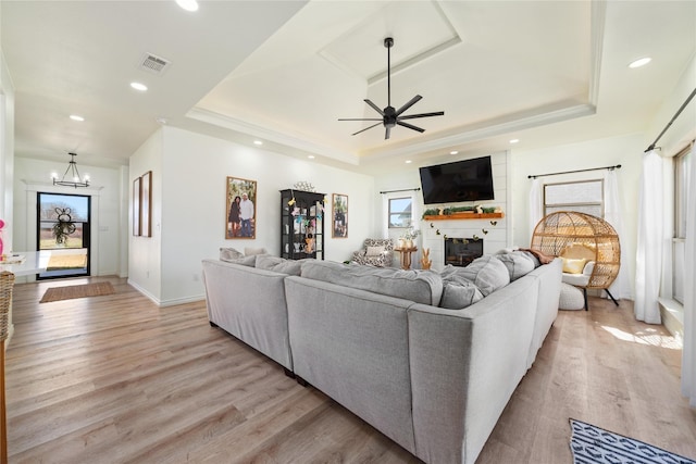 living room featuring light wood-style floors, visible vents, a fireplace, and a tray ceiling